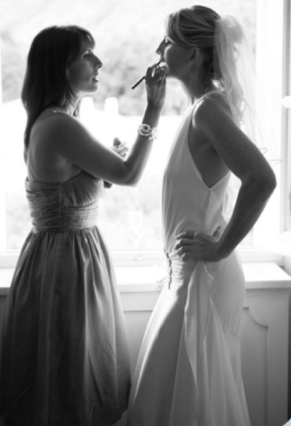 Nikki applying bridal makeup to a bride beside a bright window